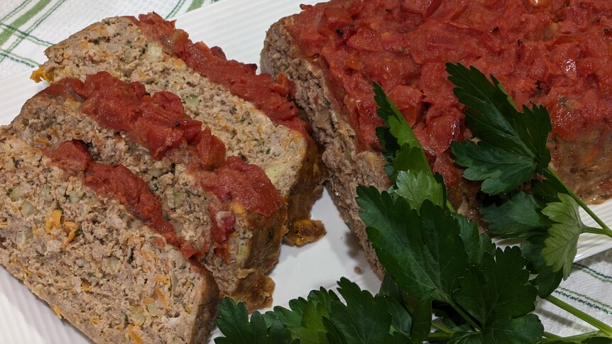 Beef and pork meatloaf topped with tomato sauce, beside three cut slices, ready to eat.