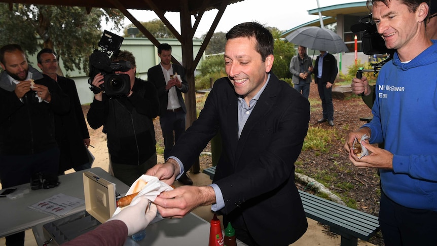 Matthew Guy hands a sausage to a voter at a barbecue.