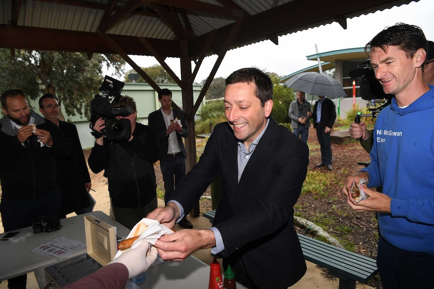 Matthew Guy hands a sausage to a voter at a barbecue.