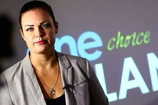 Woman in suit jacket stands in front of notice