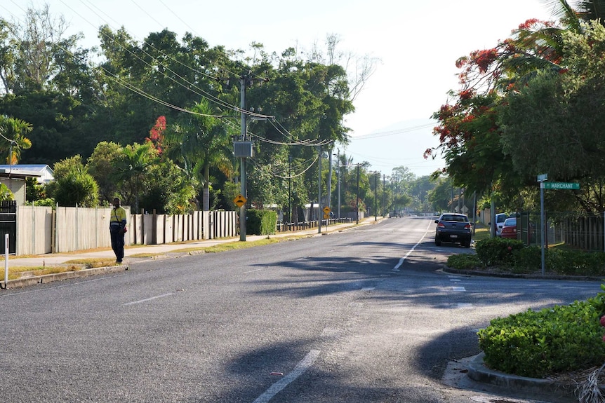 Wide shot of street. An Aboriginal man wearing hi-viz stands on the street.