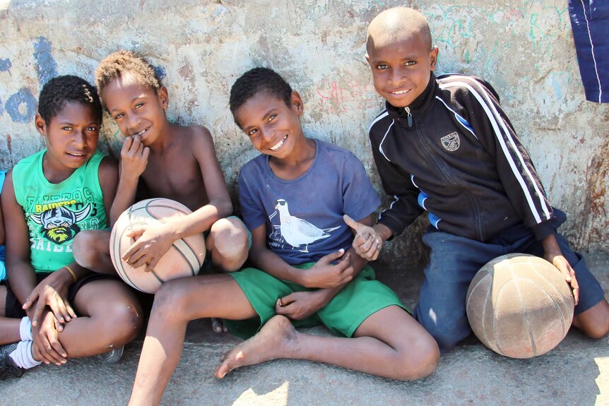 Five young PNG boys sit against a graffitied wall.