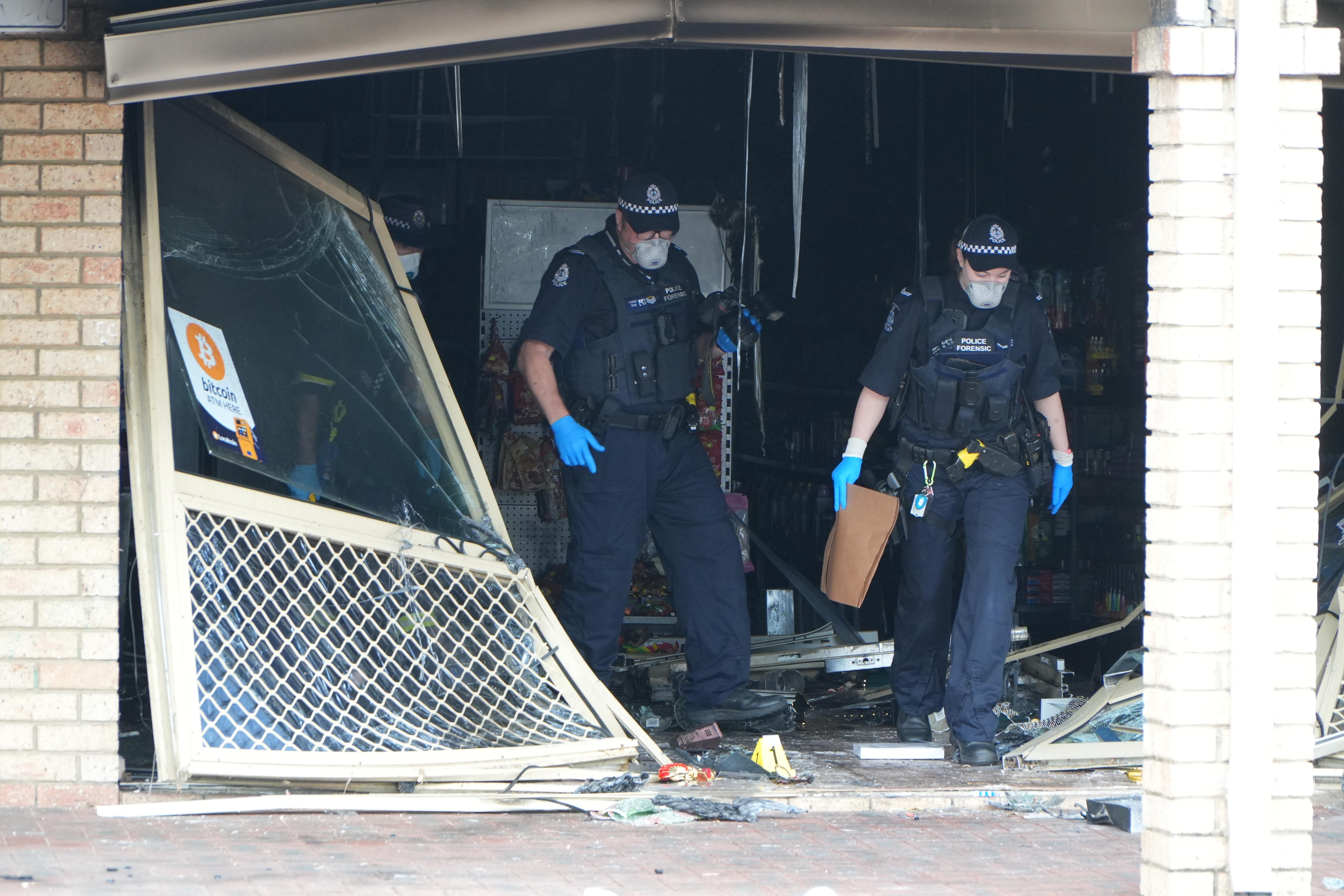 Dos agentes de policía abandonan la entrada dañada de un supermercado después de que este fuera embestido e incendiado.