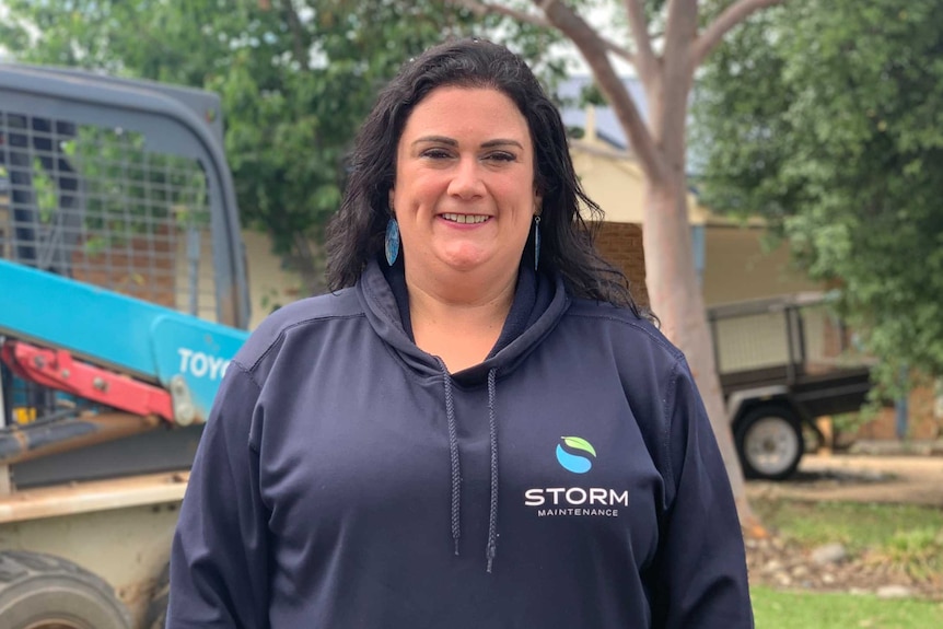 Katie Lindsay Fuimaono wearing a black hoodie and standing outdoors in front of a work vehicle.