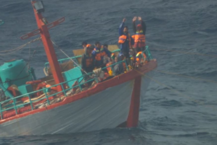 Nelayan Indonesia dengan jaket pelampung melambaikan tangan mereka di kapal yang setengah tenggelam
