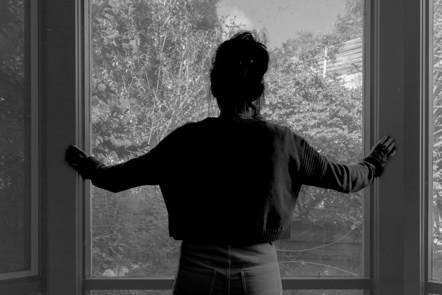 A woman looks out a window toward a garden.