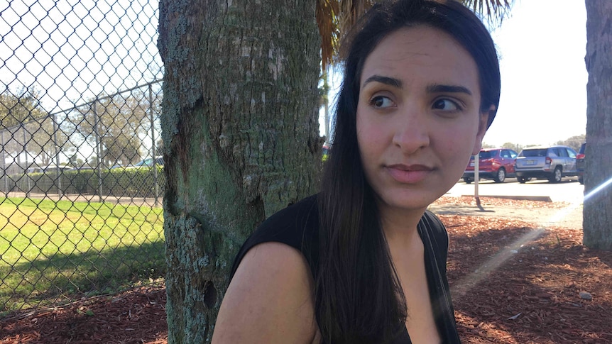 A woman sits beneath a tree. She's looking off camera and not smiling.