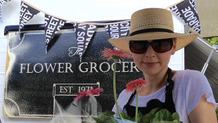 A lady stands with flowers in front of a vintage caravan