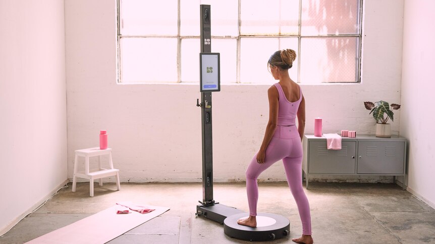 A woman in active sweat-gear lunges onto a circular raised platform attached to a high-tech scanning pole.