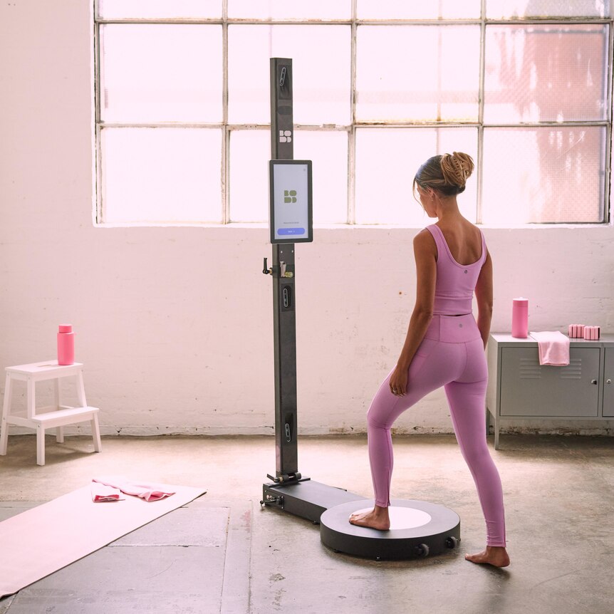 A woman in active sweat-gear lunges onto a circular raised platform attached to a high-tech scanning pole.