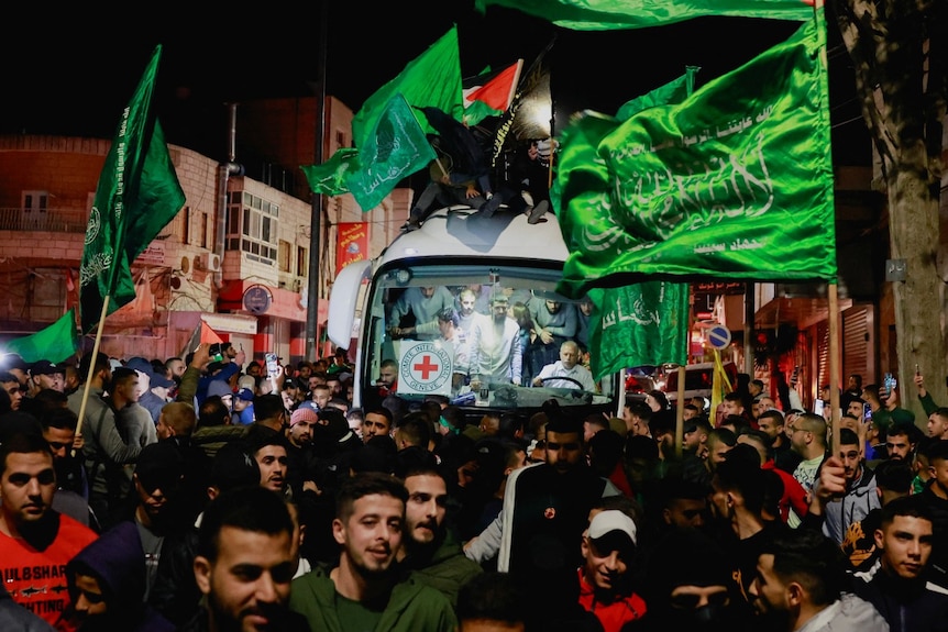 A large number of people, including some waving green flags, near a bus at night