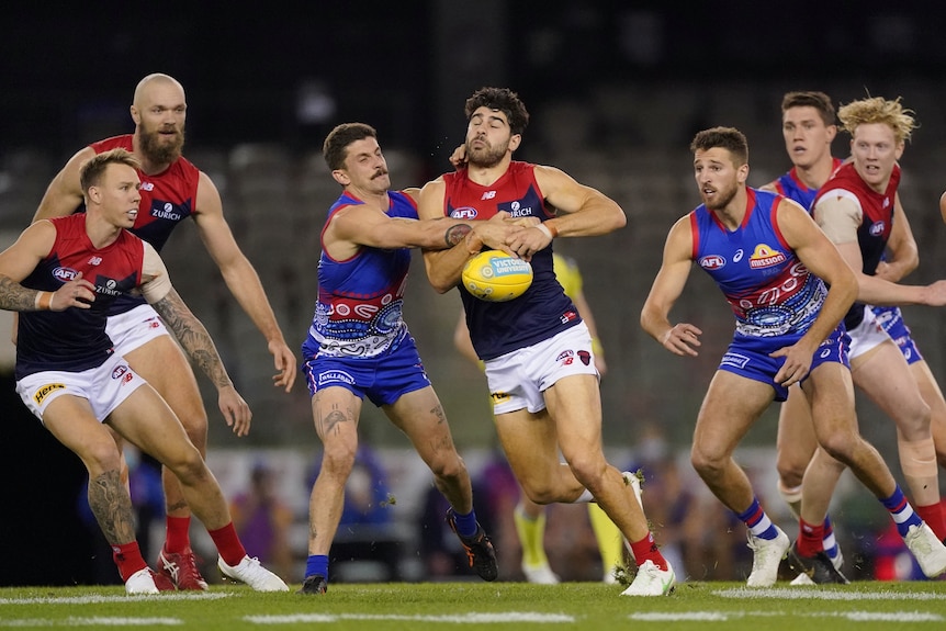 Two Aussie rules players fighting for the ball with both teams surrounding them during a match