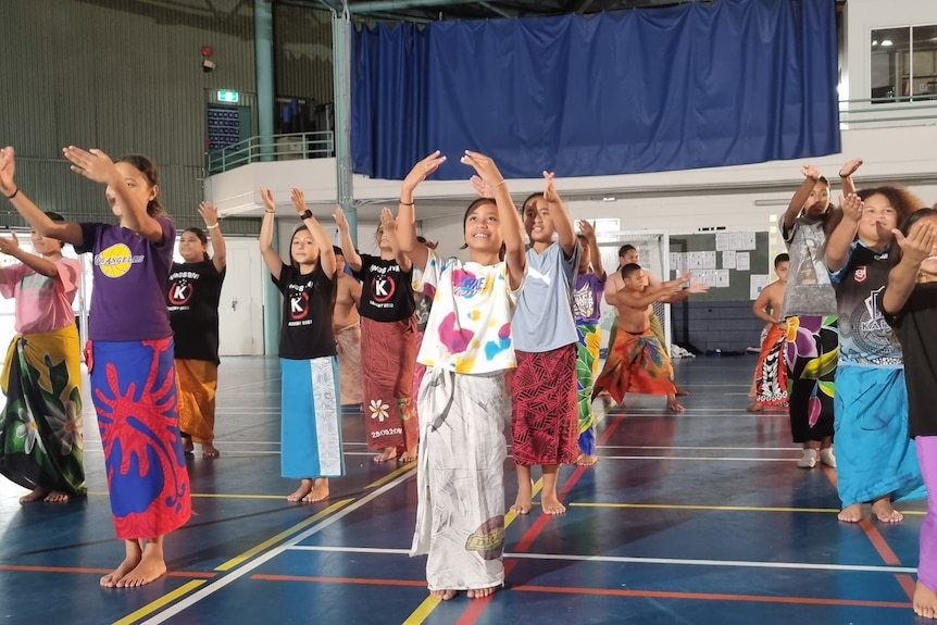 Rows of young Samoan children wear their ie lavalava and dance in blue school hall