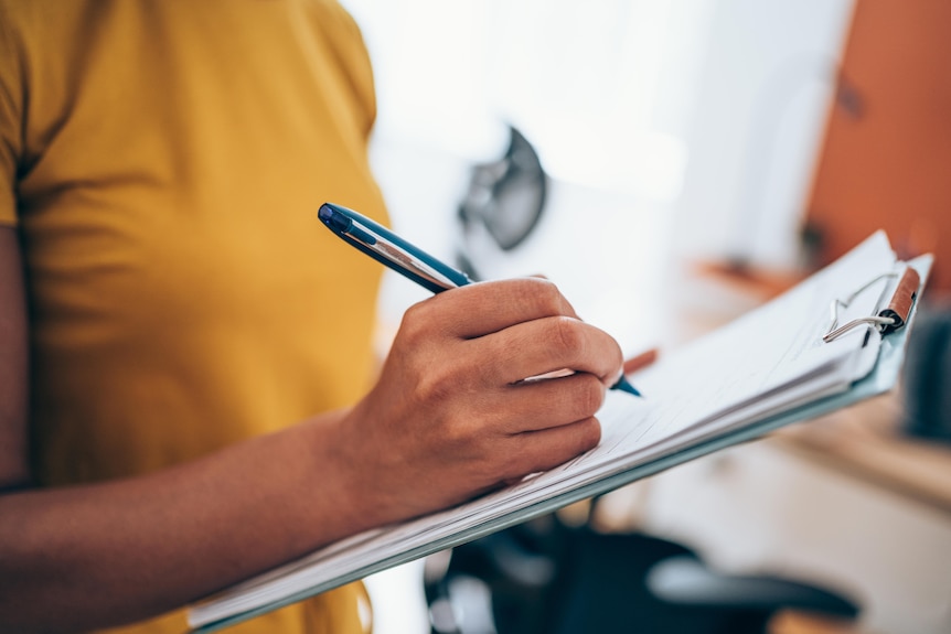 A woman in a yellow t-shirt holds a contract clipped to a clipboard and a pen.