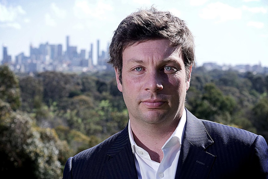 Tim Smith poses for a portrait, with CBD skyscrapers in the far background
