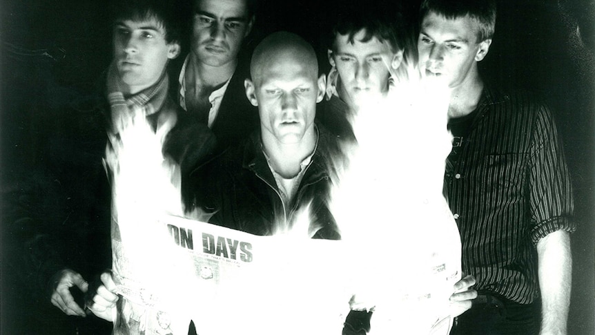 A black and white promo photo of Midnight Oil holding a burning newspaper