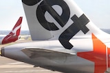 A Qantas jet passes a Jetstar plane, the logos on their tails visible.