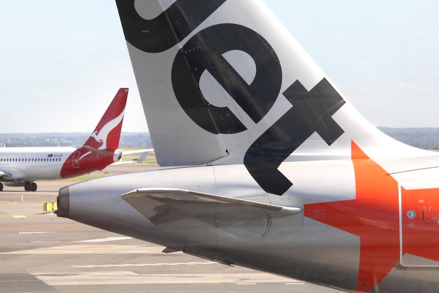 A Qantas jet passes a Jetstar plane, the logos on their tails visible.