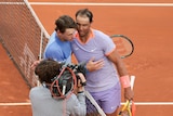 Two men hug at a tennis net on an orange clay court.