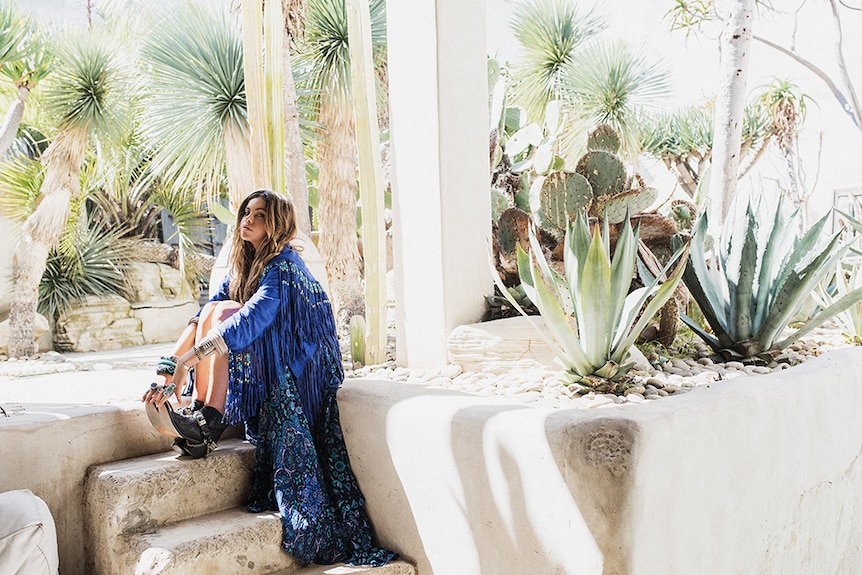 Model in blue tasselled jacket sitting on steps near cactus garden