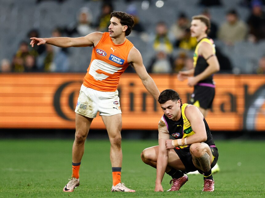 A GWS AFL player stands on the ground pointing down the field, while a Richmond player crouches recovering from a tackle.