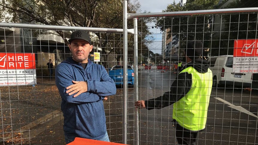 A man wearing a cap stands next to a wire fence.