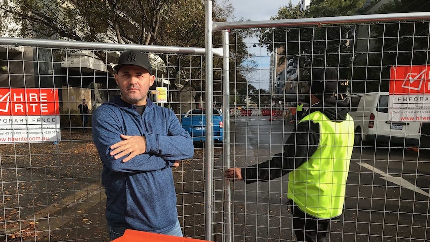 A man wearing a cap stands next to a wire fence.