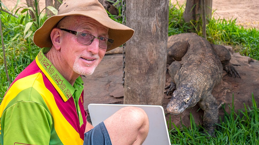 A man wearing a floppy hat with a Komodo dragon behind him.