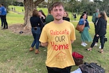 A young man wearing a bright-coloured shirt with the slogan "relocate our homes" painted on the front.