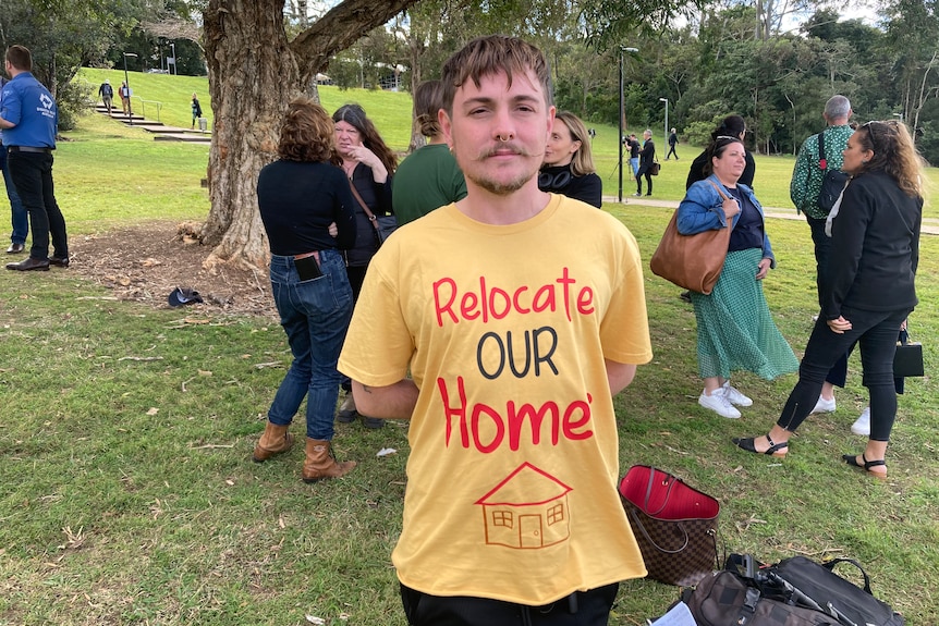 A young man stands in a yellow shirt with the slogan 'relocate our homes' hand painted on the front.