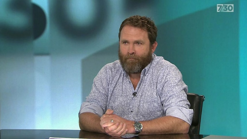 A man sits at a table in a TV studio