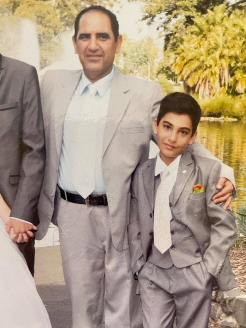 A young child and a older man wearing suits in front of a lake