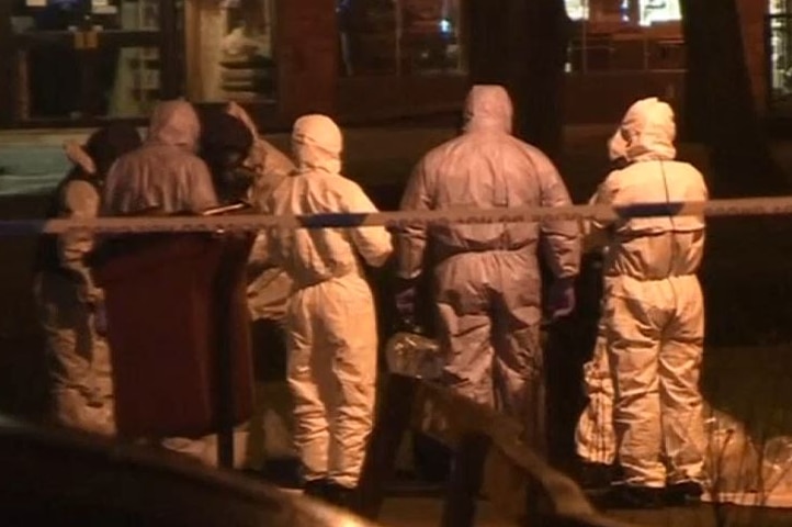 People wearing Hazmat suits stand in a group on a street.