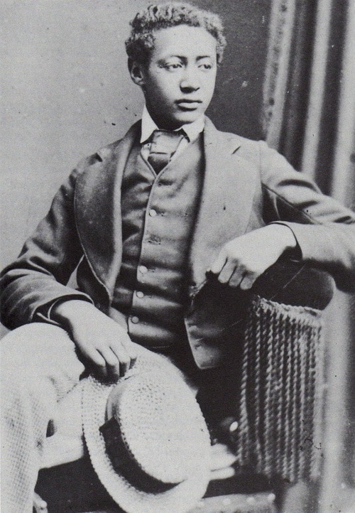Black and white portrait of Alemayehu as a teenager wearing a suit and tie. His hair hair is combed to a side.