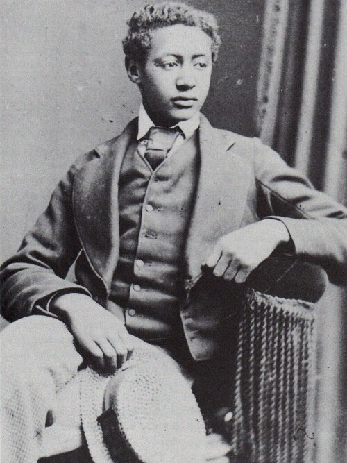 Black and white portrait of Alamayu as a teenager wearing a suit and tie. His hair hair is combed to a side.