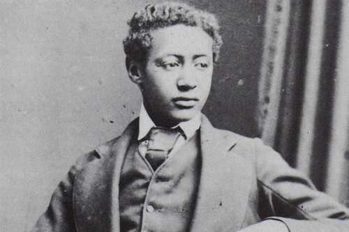 Black and white portrait of Alemayehu as a teenager wearing a suit and tie. His hair hair is combed to a side.