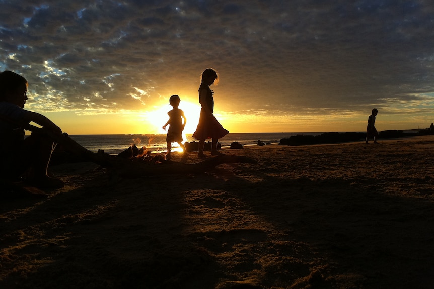 Silhouette of Indigenous children on a beach at sunset.