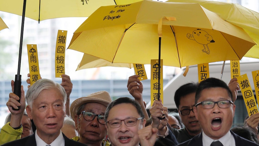 A group of men shouting with yellow signs and umbrellas behind them