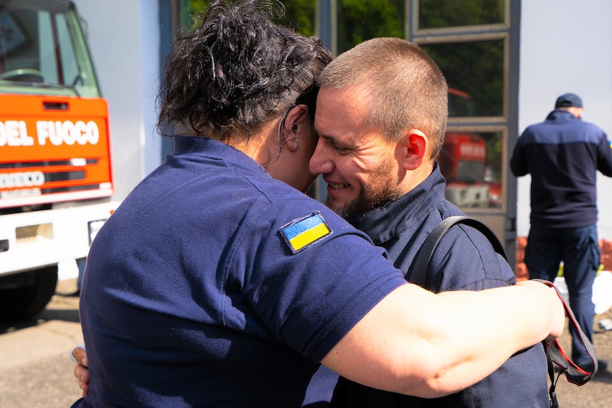 A man and a woman wearing blue uniforms with the Ukrainian flag hug.