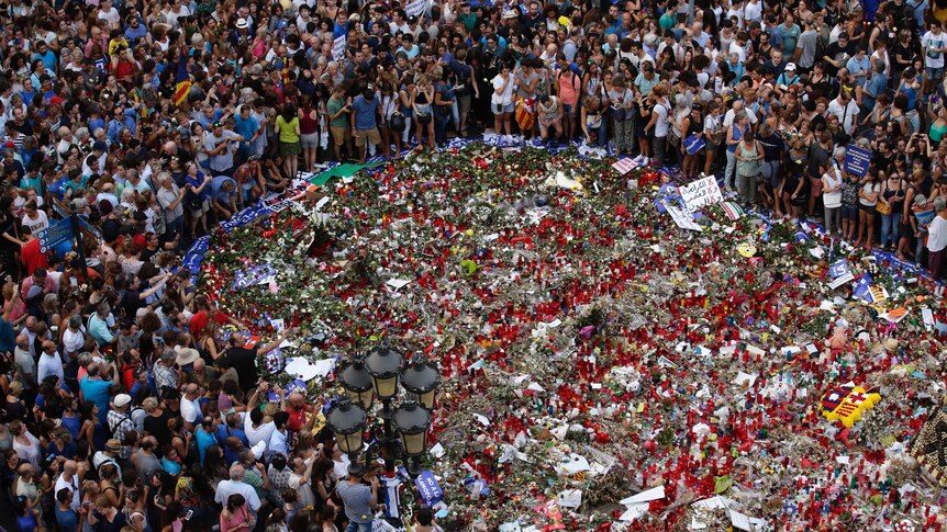 Hundreds of people gathered in a circle around a tribute of flowers laid on Las Ramblas.