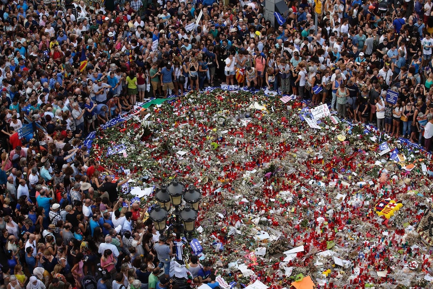 Hundreds of people gathered in a circle around a tribute of flowers laid on Las Ramblas.