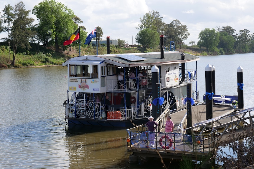 People gather on a paddle wheel boat docked on a river