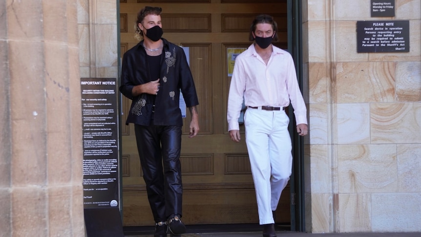 A man wearing black and a man wearing a pink shirt and white pants leaving a court door