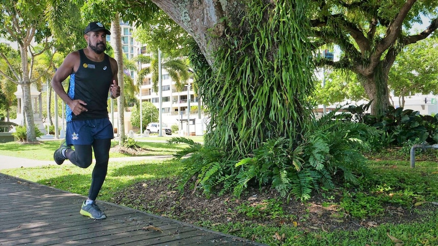 Indigenous man in cap, singlet and shorts jogging on tree-lined path