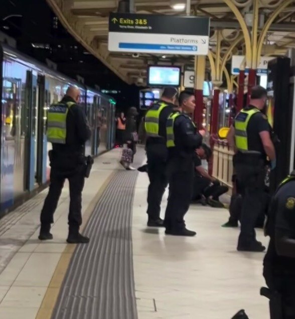 A number of police officers in navy uniforms with bright yellow vests stand on a platform beside a train at night.