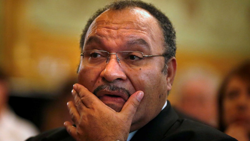 A Papua New Guinean man in glasses and a gold bracelet touches his face