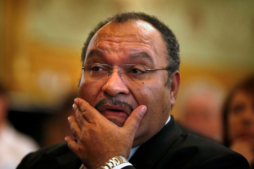 A Papua New Guinean man in glasses and a gold bracelet touches his face