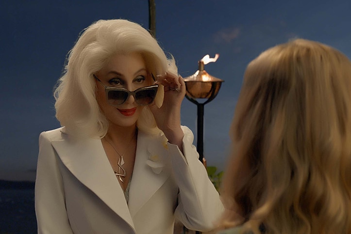 Colour still image from 2018 film Mamma Mia! Here We Go Again of Cher looking over sunglasses at Amanda Seyfried in the evening.