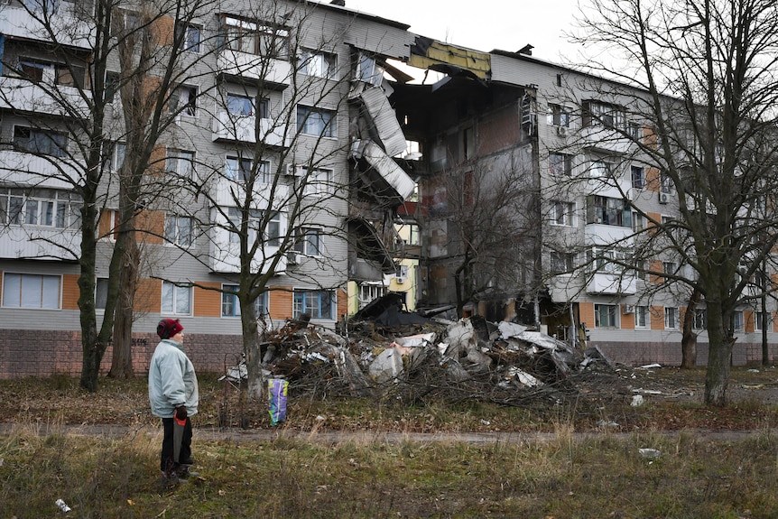 A woman is pictured looking at an apartment building that has been severely damaged by shelling.