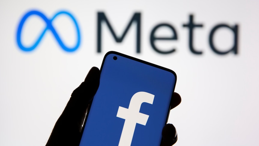 A smartphone with Facebook's logo is seen in front of displayed Facebook's new rebrand logo Meta.